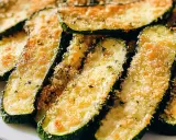 Fette di zucchine gratinate in padella, dorate e croccanti, con pangrattato e erbe aromatiche.