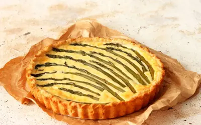 Torta salata asparagi con crosta dorata e ripieno cremoso, decorata con asparagi freschi disposti a raggiera.
