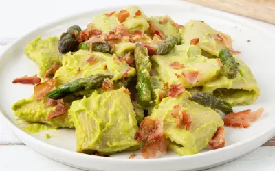 Piatto di pasta con crema di asparagi, punte di asparagi freschi e croccante speck.