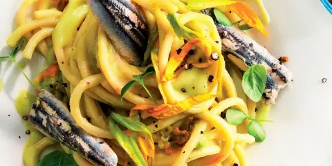 Pasta con fiori di zucca e alici, un piatto estivo colorato e saporito, con erbe fresche e pepe nero.