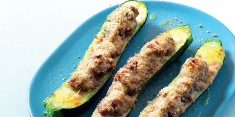 Tre zucchine ripiene, dorate e gratinate, servite su un piatto blu. Un piatto invitante e saporito.