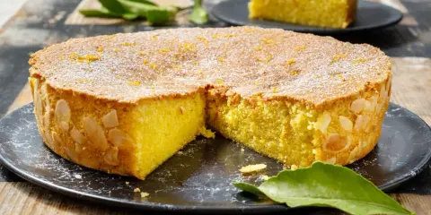 Deliziosa caprese al limone, con mandorle tostate sui bordi e scorzetta d'arancia in superficie, cosparsa di zucchero a velo.