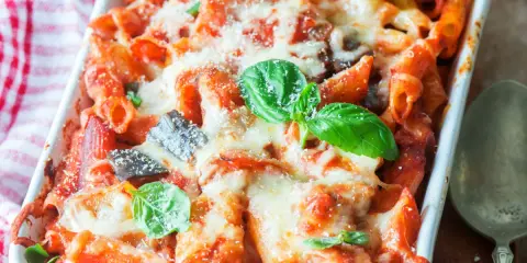 Penne al forno con melanzane, pomodoro e abbondante formaggio filante, guarnite con basilico fresco.