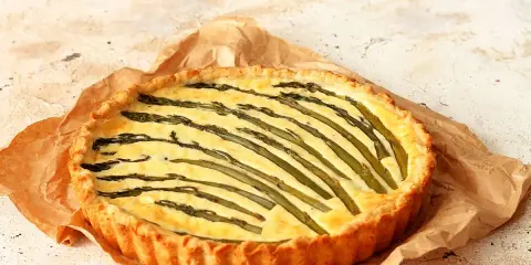 Torta salata asparagi con crosta dorata e ripieno cremoso, decorata con asparagi freschi disposti a raggiera.