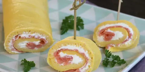 Rotolo di frittata ripieno di salmone affumicato e formaggio cremoso, guarnito con prezzemolo. Un antipasto elegante e gustoso.
