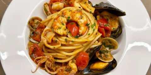 Un invitante piatto di spaghetti allo scoglio, con gamberi, cozze, vongole e calamari, condito con pomodorini e prezzemolo.