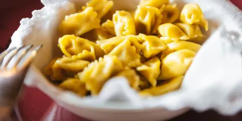 Un primo piatto invitante: tanti ravioli del plin dorati, serviti in una ciotola bordata di bianco.