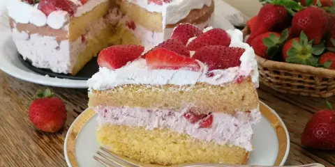Una fetta di torta mascarpone e fragole, con strati di pan di spagna, crema rosa e fragole fresche, guarnita con panna e fragole.