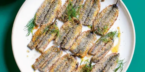 Piatto di alici al forno dorate e croccanti, guarnite con finocchietto fresco e un filo d'olio.
