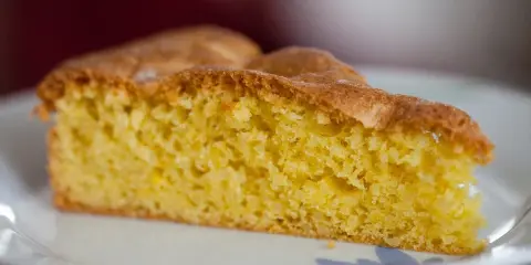 Una fetta di torta soffice e dorata, preparata con farina di mandorle, su un piatto bianco.