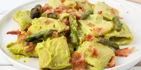 Piatto di pasta con crema di asparagi, punte di asparagi freschi e croccante speck.