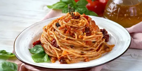 Spaghetti con pomodori secchi, basilico fresco e un filo d'olio d'oliva. Un piatto semplice e gustoso, pronto per essere assaporato.