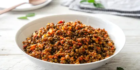 Un piatto invitante di lenticchie in umido, condite con pomodoro e cipolla, servite in una ciotola bianca su un tavolo di legno.