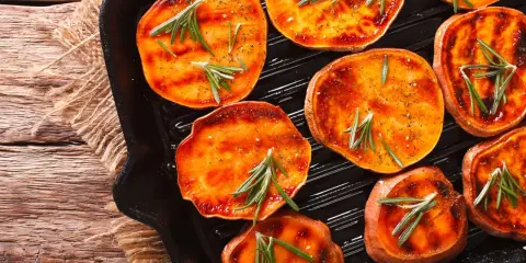 Fette di patate dolci grigliate in padella, condite con rosmarino e spezie, pronte per essere gustate.