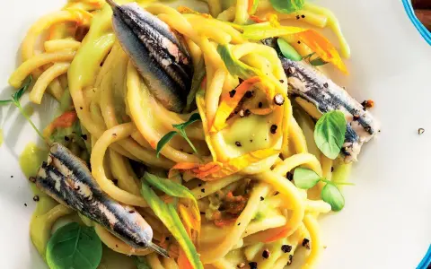 Pasta con fiori di zucca e alici, un piatto estivo colorato e saporito, con erbe fresche e pepe nero.