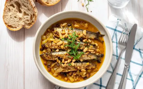 Sarde in saor, un piatto veneziano con sarde, cipolle, pinoli e uvetta, servito in una ciotola con pane rustico.
