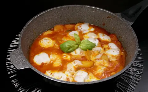 Patate alla pizzaiola in padella, con mozzarella filante e basilico fresco. Un piatto gustoso e invitante.