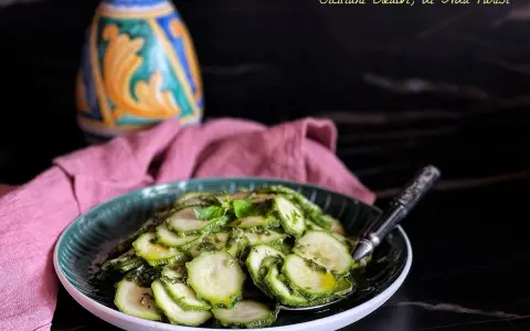 Fetta di zucchine marinate crude condite con erbe aromatiche e olio, servite su un piatto verde.