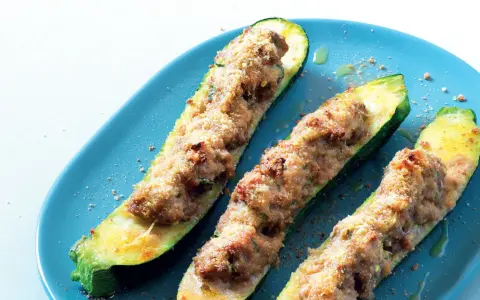Tre zucchine ripiene, dorate e gratinate, servite su un piatto blu. Un piatto invitante e saporito.
