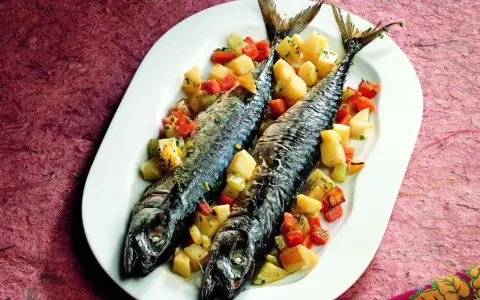 Due filetti di sgombro al forno, cotti alla perfezione, serviti con patate e carote a cubetti su un piatto bianco.