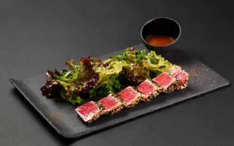Tataki di tonno scottato, servito con insalata fresca e una ciotolina di salsa.
