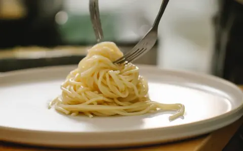 Spaghetti al limone serviti su un piatto bianco, con due forchette che raccolgono la pasta.