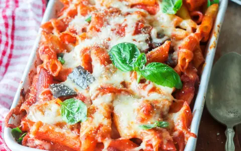 Penne al forno con melanzane, pomodoro e abbondante formaggio filante, guarnite con basilico fresco.