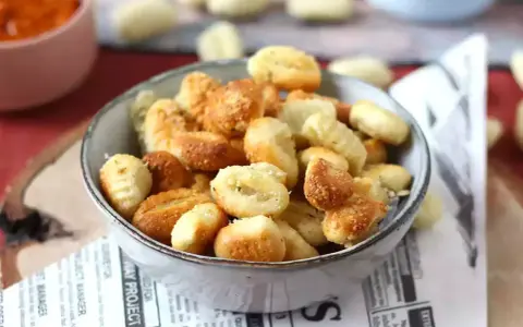 Gnocchi dorati e croccanti in friggitrice ad aria, serviti in una ciotola su carta di giornale.