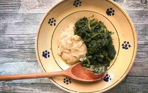 Piatto rustico con fave e cicoria, un classico della cucina italiana, servito su un piatto decorato con fiori blu.