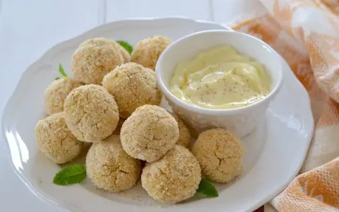 Polpette di ceci al forno dorate e croccanti, servite su un piatto bianco con una ciotolina di salsa cremosa e foglie di menta.