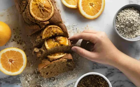Un profumato plumcake all'arancia, uno dei tanti dolci senza glutine, pronto per essere gustato. Accanto, arance fresche e avena.