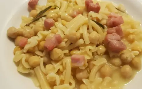 Un piatto di pasta e ceci in scatola, arricchito da cubetti di pancetta e un rametto di rosmarino.