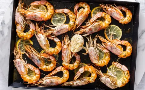 Gamberoni al forno dorati e succulenti, conditi con erbe aromatiche e spicchi di limone, pronti per essere gustati.
