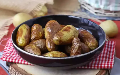 Patate novelle dorate e croccanti, appena sfornate dalla friggitrice ad aria, servite in una ciotola scura su un tagliere di legno.