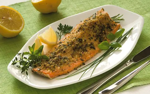 Deliziosa trota salmonata al forno, croccante e profumata, servita con limone e erbe aromatiche fresche.