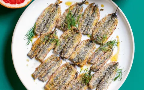 Piatto di alici al forno dorate e croccanti, guarnite con finocchietto fresco e un filo d'olio.