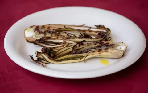 Radicchio in padella, grigliato e caramellato, servito su un piatto bianco con un filo d'olio.