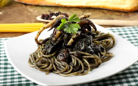 Un piatto invitante di spaghetti al nero di seppia, con tentacoli di calamaro e prezzemolo fresco, su una tovaglia a quadri verdi.