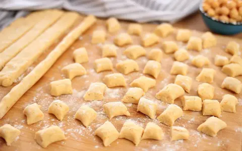 Piccoli gnocchi di ceci sparsi su un tagliere di legno, pronti per essere cotti.