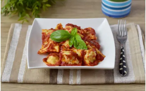 Un piatto di ravioli di carne conditi con sugo rosso e basilico fresco, pronti per essere gustati.