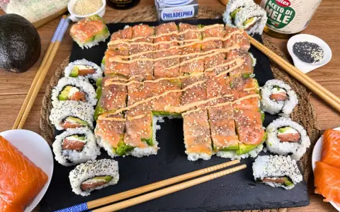 Un invitante sushi fatto in casa con salmone e avocado, guarnito con semi di sesamo e una salsa cremosa.