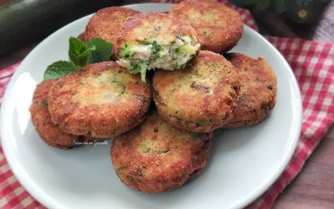 Piatto di polpette di zucchine e ricotta dorate e croccanti, guarnite con menta fresca.
