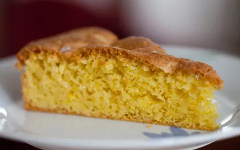 Una fetta di torta soffice e dorata, preparata con farina di mandorle, su un piatto bianco.