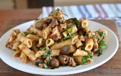 Piatto di pasta al tonno con olive verdi e prezzemolo fresco, servita su un piatto bianco.