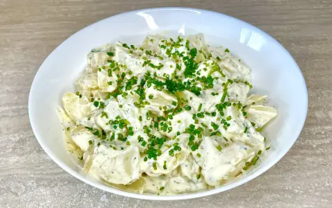 Una cremosa insalata di patate, condita con erbe aromatiche e guarnita con erba cipollina fresca. Perfetta per un picnic o un pranzo leggero.
