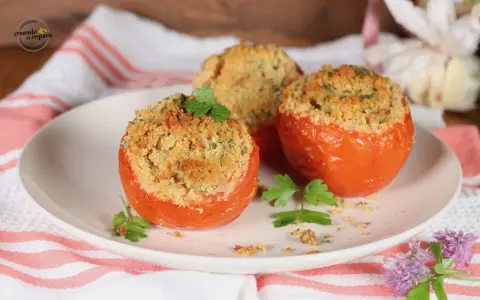 Tre pomodori gratinati al forno, ripieni e dorati, guarniti con prezzemolo fresco su un piatto bianco.