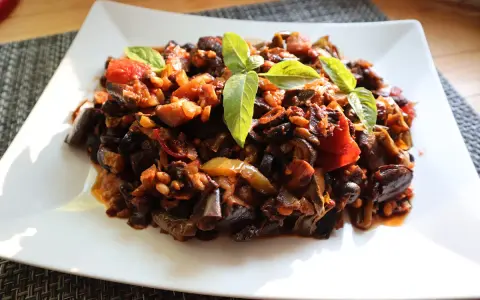 Un piatto di saporita caponata di melanzane, guarnita con foglie di basilico fresco.