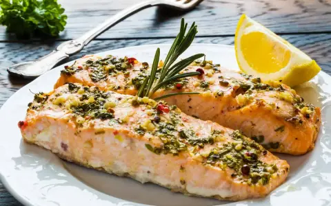 Delizioso salmone al forno con erbe aromatiche, aglio e peperoncino, guarnito con rosmarino e una fetta di limone.
