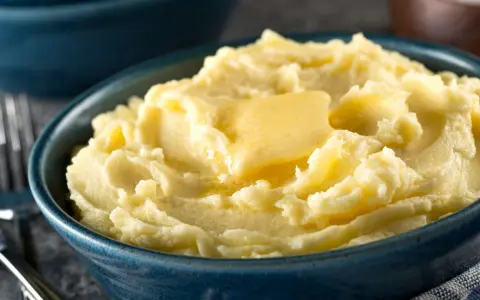 Una ciotola blu piena di soffice purea di patate, con una fetta di burro che si scioglie sopra.