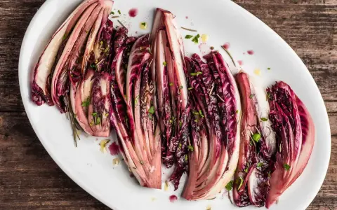 Radicchio al forno, tagliato a spicchi e condito con erbe aromatiche, servito su un piatto bianco.